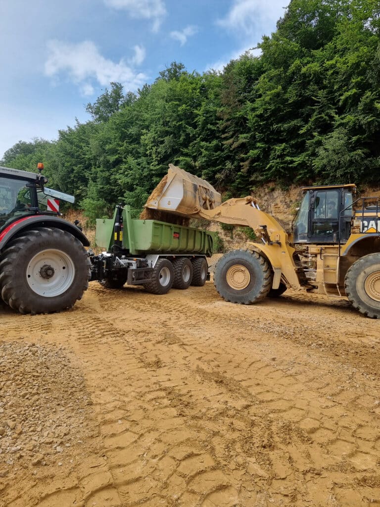 Une pelle qui déverse de la terre dans une benne remorquée à un tracteur.