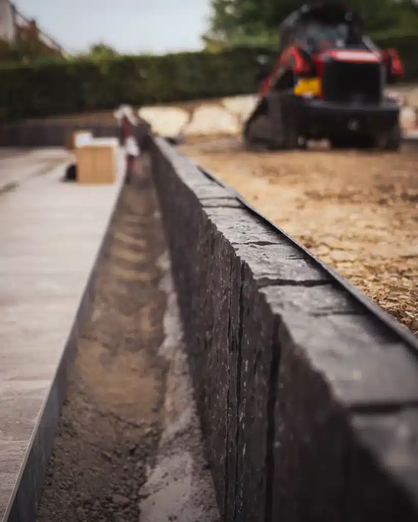 Gros plan sur l'installation d'une bordure d'une terrasse en pierres noires.